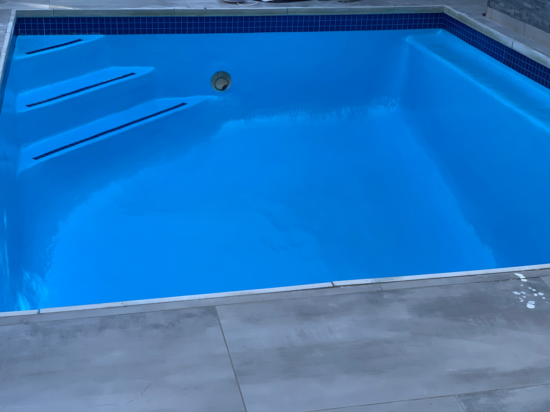 Freshly relined swimming pool with bright blue finish and dark blue mosaic tiles