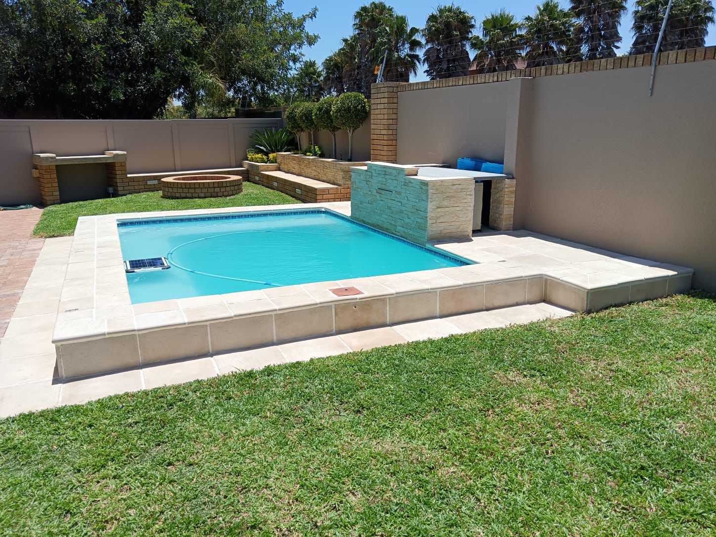 Completed backyard pool with paved surround, fire pit and braai area