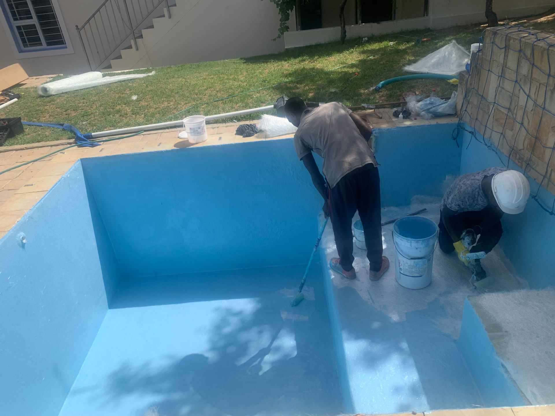 Workers applying a bright blue fibreglass lining inside an empty swimming pool